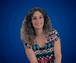 Débora Slotnisky, con expresión amigable, cabello rizado suelto y vestido colorido con formas geométricas, sobre un fondo azul liso.