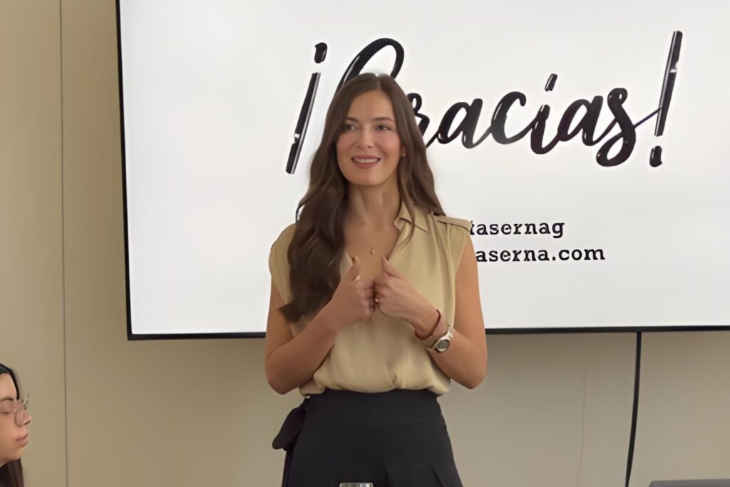 Fotografía de Catalina Serna finalizando una conferencia, sonriendo frente a una pantalla con la palabra “¡Gracias!”, en un ambiente profesional.