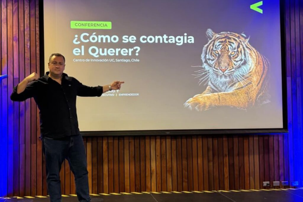 Fotografía de Felipe Peña y Lillo durante su conferencia “¿Cómo se contagia el Querer?” en el Centro de Innovación UC, Santiago de Chile, acompañado de una proyección con la imagen de un tigre.