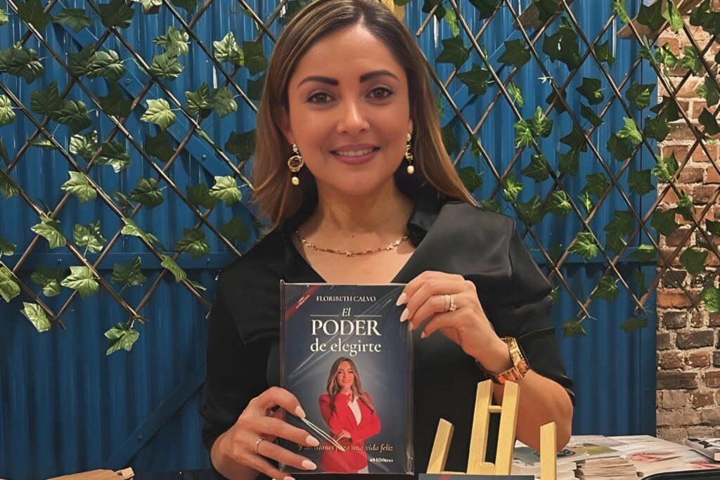Fotografía de Floribeth Calvo sosteniendo su libro “El Poder de Elegirte”, posando con una sonrisa en un entorno decorado con plantas.