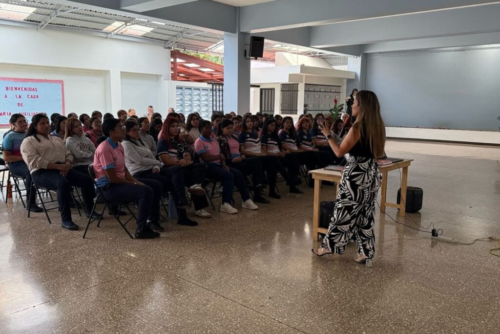 Fotografía de Floribeth Calvo impartiendo una charla motivacional a un auditorio lleno de estudiantes, quienes escuchan con atención en un salón amplio.