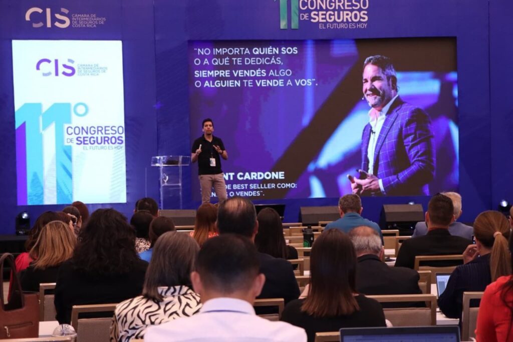 Fotografía de Patricio García impartiendo una conferencia en el 11° Congreso de Seguros de Costa Rica, con una pantalla gigante mostrando una cita de Grant Cardone.