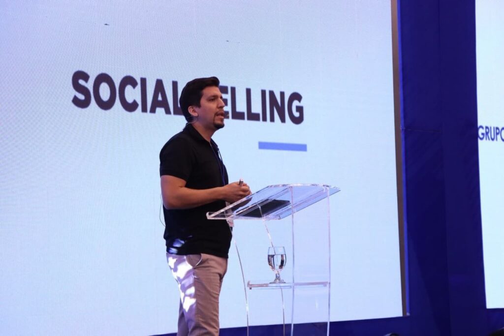 Fotografía de Patricio García impartiendo una conferencia sobre Social Selling, de pie junto a un atril transparente con proyector de fondo.