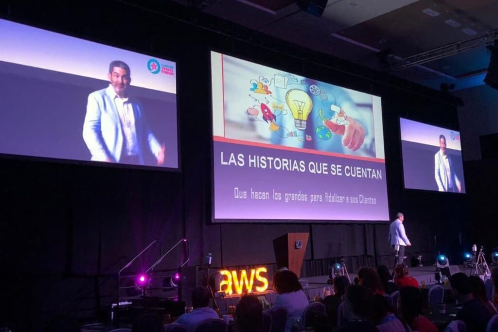Fotografía de Pedro Eloy dando una conferencia en el Caribe Travel Forum, con una pantalla gigante detrás que muestra el tema “Las historias que se cuentan: Qué hacen los grandes para fidelizar a sus clientes”.