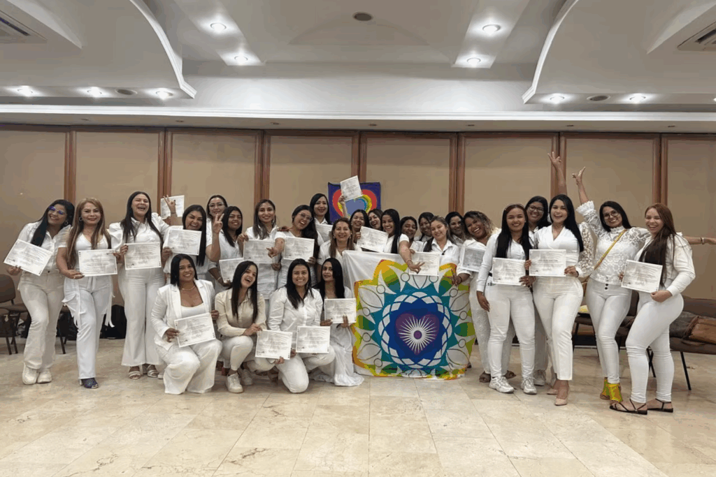 Fotografía de Liry Matallana con un grupo de mujeres vestidas de blanco, mostrando orgullosamente sus certificados de formación en un evento de crecimiento personal y liderazgo.