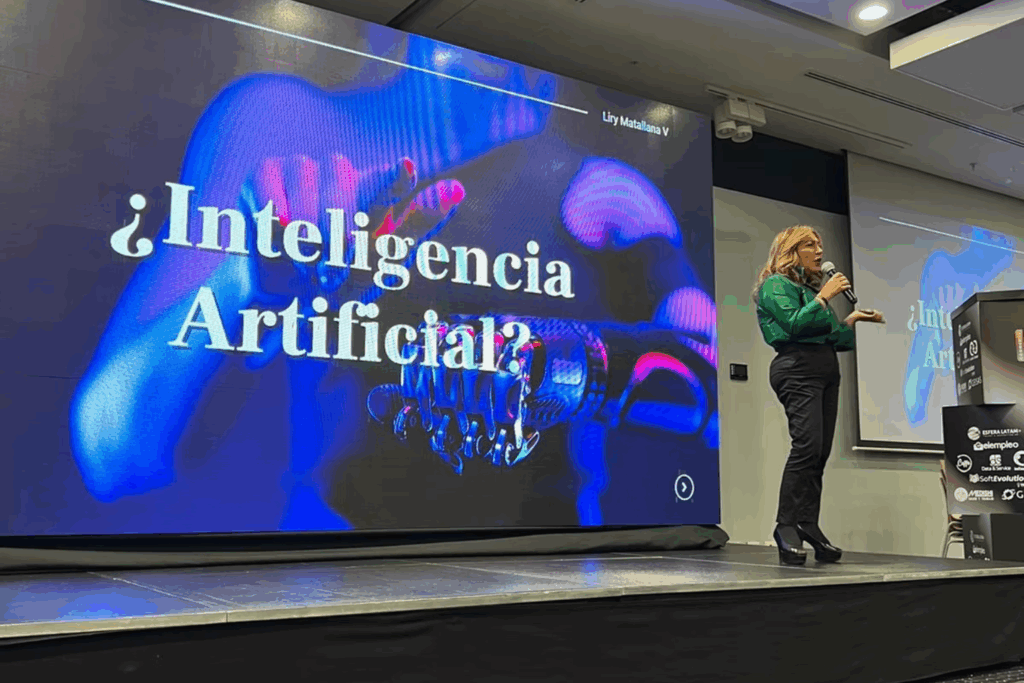 Fotografía de Liry Matallana en un escenario, dando una conferencia sobre inteligencia artificial frente a una gran pantalla con gráficos tecnológicos.