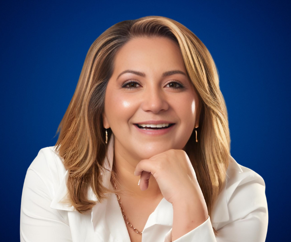 Fotografía de Liry Mantallana sonriendo con expresión cálida y cercana, vistiendo blusa blanca sobre fondo azul.