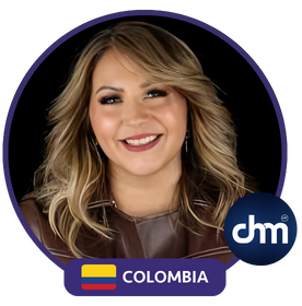 Fotografía de Liry Mantallana sonriendo con expresión cálida, luciendo chaqueta marrón sobre fondo oscuro, con el distintivo de Colombia.