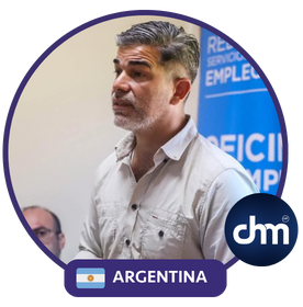 Lucas Romero Sosa hablando en un entorno institucional, vistiendo camisa clara, con fondo de banners azules y el logo de dhm Argentina visible en primer plano.