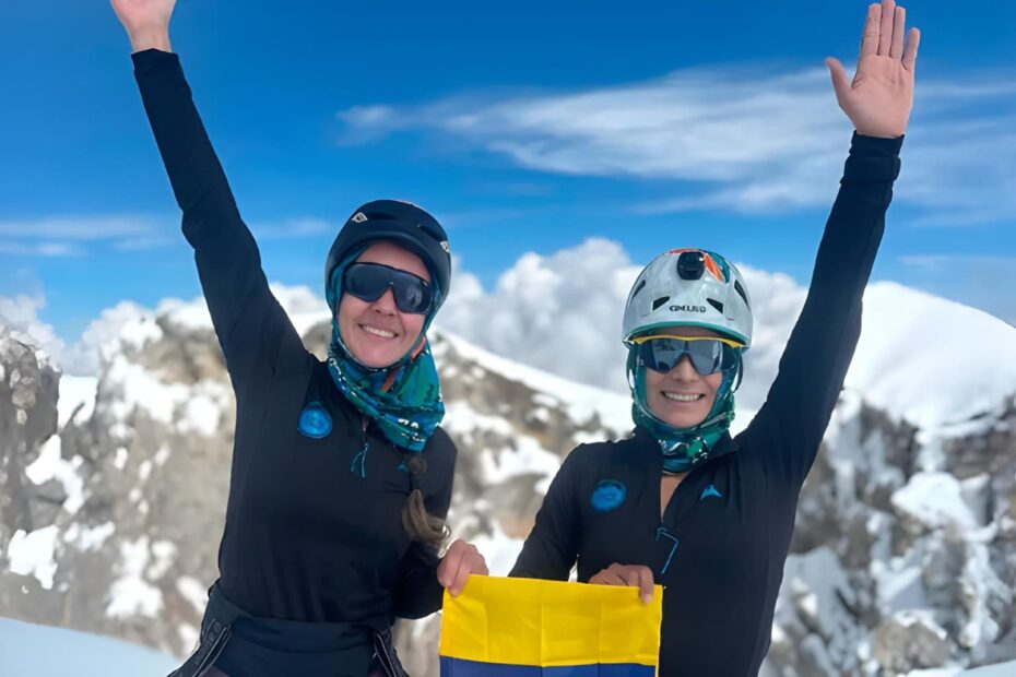 Dos montañistas colombianas celebrando en la cima de una montaña nevada, en su camino hacia completar el reto de las 7 Cumbres.