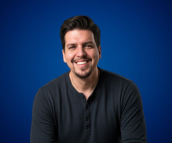 Fotografía de Patricio Garcia sonriendo frente a un fondo azul sólido, con iluminación profesional y vestimenta casual oscura.