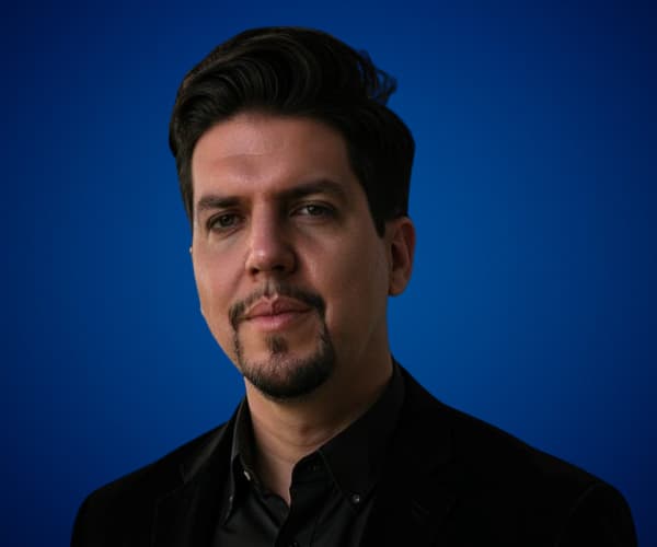 Fotografía de Patricio García con fondo azul, vistiendo traje oscuro y mostrando una expresión seria y profesional en un retrato de estudio.