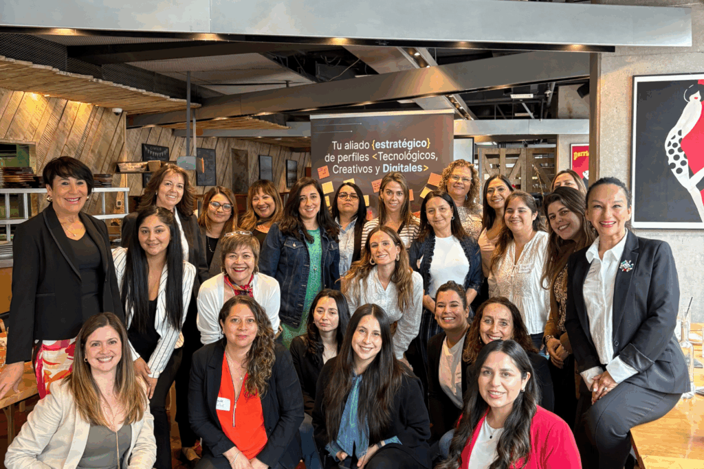 Fotografía de Carolina Pinto Grez junto a un grupo de mujeres profesionales en un encuentro de networking, todas sonrientes en un restaurante moderno con fondo corporativo que destaca perfiles tecnológicos, creativos y digitales.