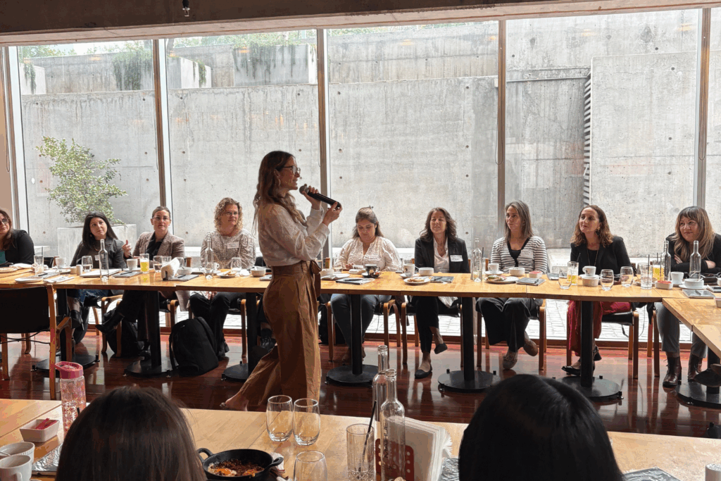 Fotografía de Carolina Pinto Grez ofreciendo una charla ante un grupo de mujeres sentadas en forma de U, en un espacio iluminado con luz natural y estilo contemporáneo.