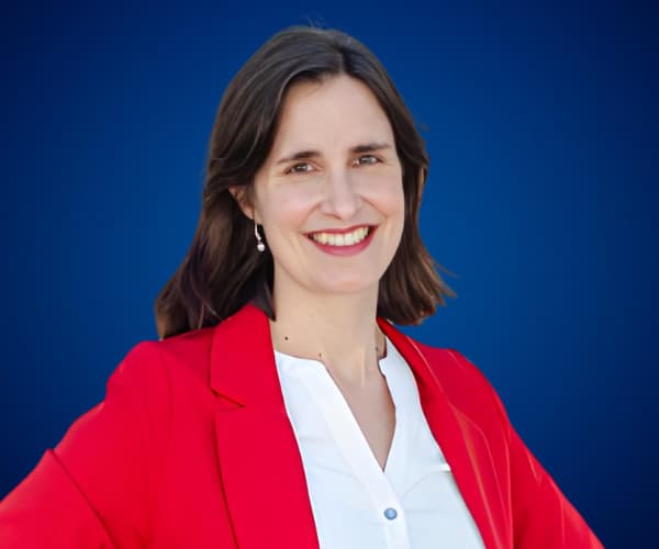 Fotografía de Ximena Hernández Buffa sonriendo, con chaqueta roja y fondo azul profesional, transmitiendo confianza y cercanía.