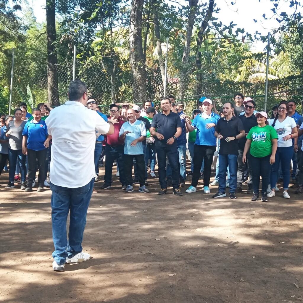 Fotografía de Rodrigo Quintanilla dirigiendo una dinámica grupal al aire libre, con un numeroso grupo de personas participando activamente en un entorno natural.