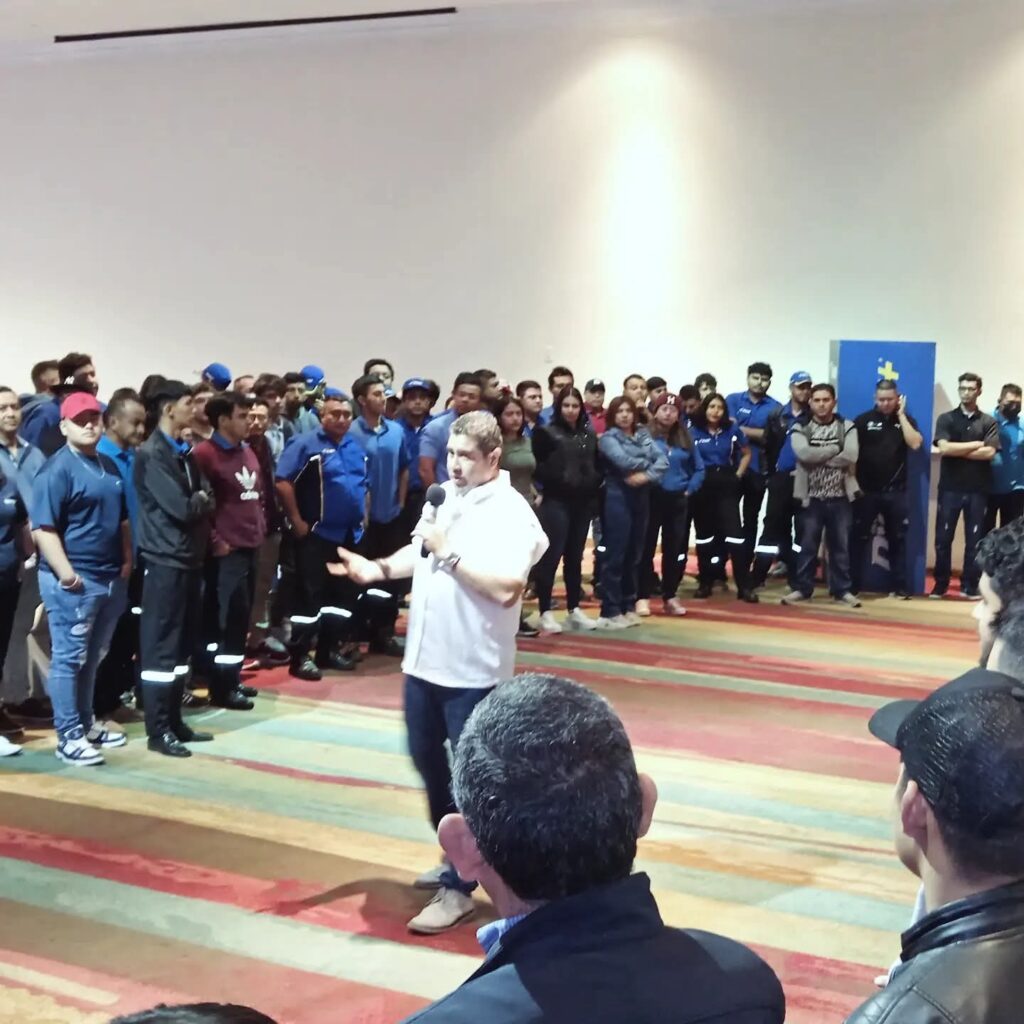 Fotografía de Rodrigo Quintanilla ofreciendo una charla motivacional en un salón amplio, rodeado de un numeroso grupo de trabajadores atentos, en su mayoría vestidos con uniformes azules.