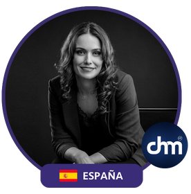 Fotografía en blanco y negro de Eva Mazuecos, sentada con expresión profesional, dentro de un marco circular con el logotipo de CHM y la bandera de España.