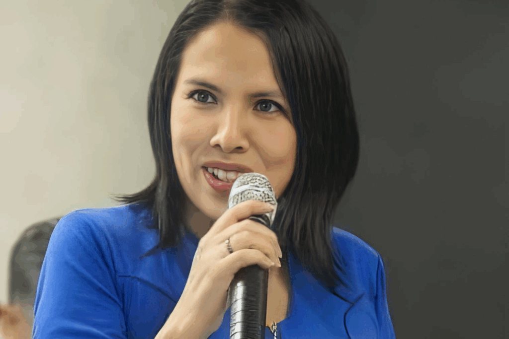 Fotografía de Erika Hernández hablando con micrófono en mano, vestida con chaqueta azul y fondo neutro, capturada en un momento de inspiración durante una conferencia.