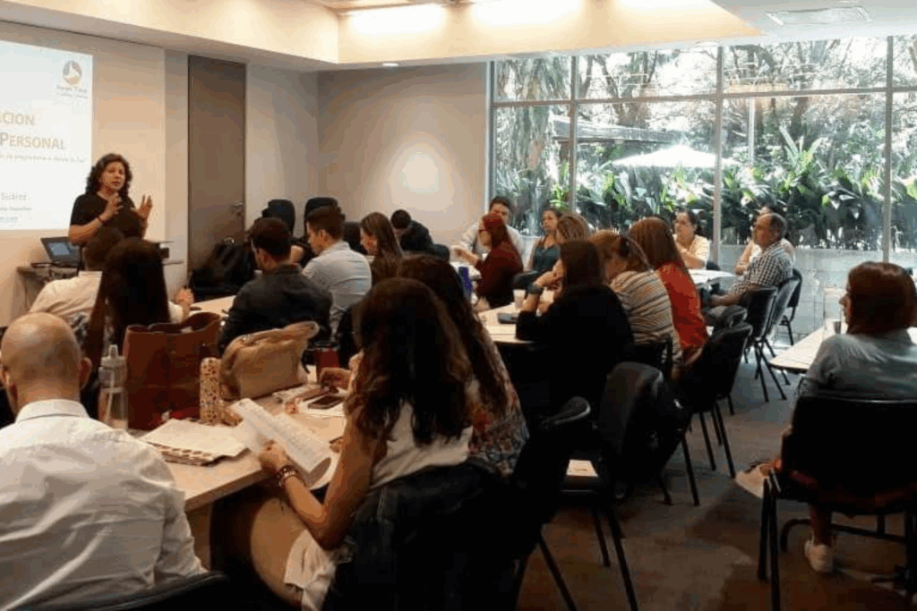 Fotografía de Lyda Ardila impartiendo una conferencia en un salón con asistentes sentados, proyectando diapositivas y generando un ambiente de aprendizaje profesional.