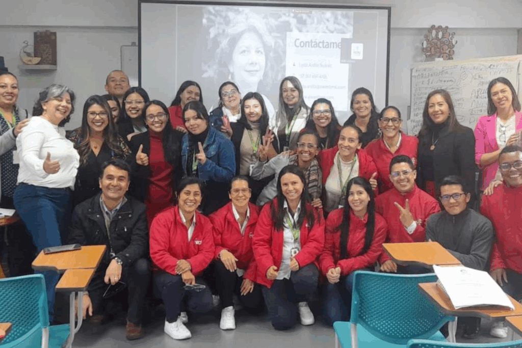 Fotografía de Lyda Ardila posando con un grupo de participantes en un taller, todos sonriendo frente a una pantalla de presentación en un aula.