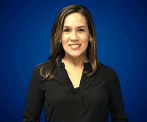 Fotografía de Nadia Vado, sonriendo frente a un fondo azul liso, vestida con blusa negra de manga larga, en un retrato profesional de medio cuerpo.