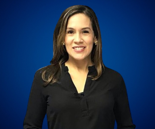 Fotografía de Nadia Vado, sonriendo frente a un fondo azul liso, vestida con blusa negra de manga larga, en un retrato profesional de medio cuerpo.
