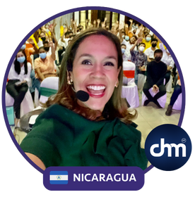 Fotografía de Nadia Vado durante una conferencia en Costa Rica, sonriendo con micrófono de diadema frente a una audiencia entusiasta con los brazos levantados, en un salón cerrado iluminado.