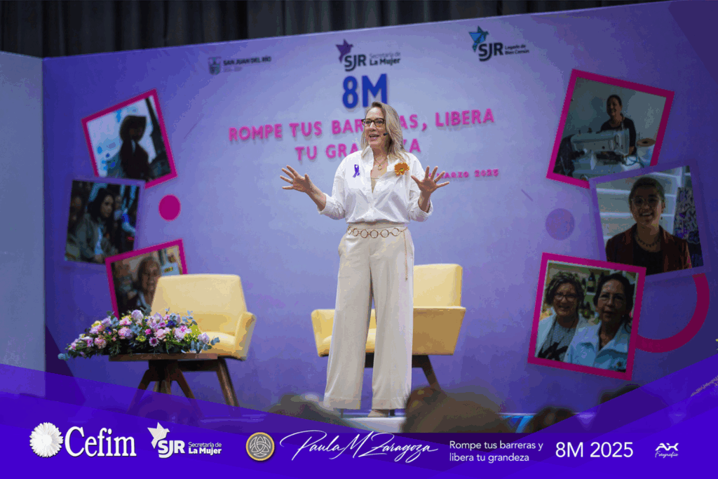Fotografía de Paula Morelos Zaragoza dando una conferencia en el marco del 8M 2025, de pie sobre el escenario con fondo púrpura que dice “Rompe tus barreras, libera tu grandeza”, vistiendo camisa blanca y pantalón claro.