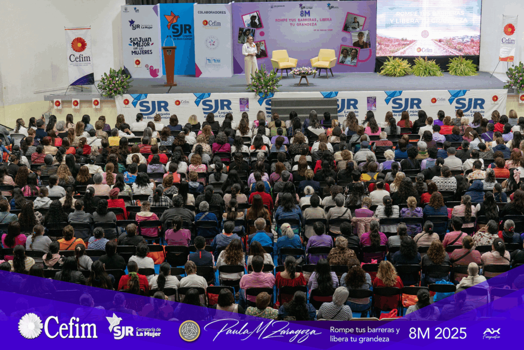 Fotografía de Paula Morelos Zaragoza impartiendo una conferencia en el 8M 2025 ante un auditorio lleno de mujeres, en un escenario decorado con el lema “Rompe tus barreras, libera tu grandeza”.