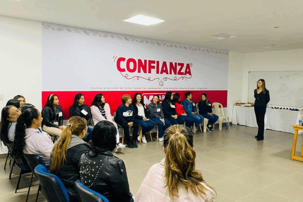 Fotografía de Sonia Rojas facilitando un taller de liderazgo y confianza, de pie frente a un grupo de participantes sentados en círculo, en un ambiente corporativo con el lema “Confianza” destacado en la pared.