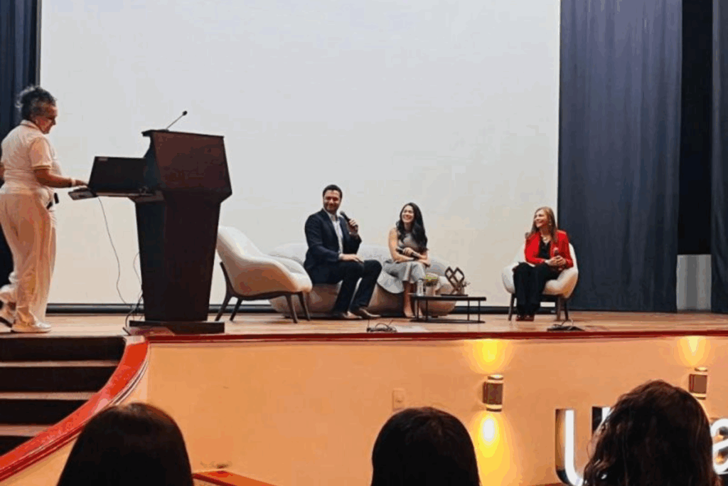 Fotografía de Sonia Rojas en un panel de conferencistas, sentada en el escenario junto a otros ponentes, frente a una audiencia en un auditorio iluminado y profesional.