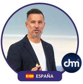 Fotografía de Rubén Montesinos durante una conferencia, vestido con saco azul oscuro y camiseta blanca, sosteniendo un control de presentación; fondo claro con el logo de CHM.