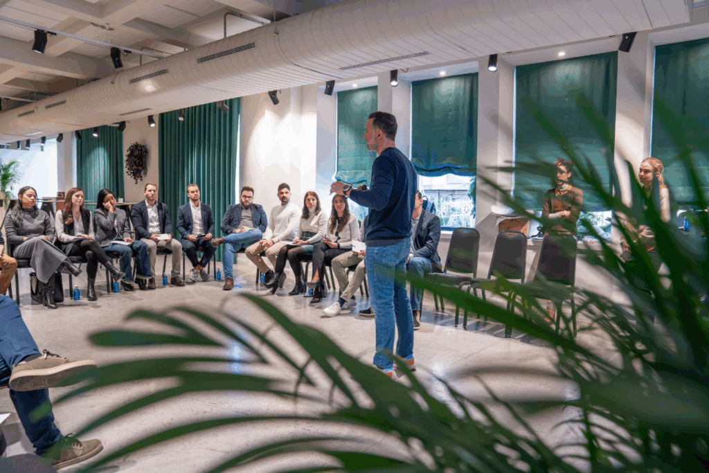 Fotografía de Rubén Montesinos facilitando una dinámica grupal en un entorno moderno y luminoso; los asistentes forman un círculo mientras lo escuchan con atención.