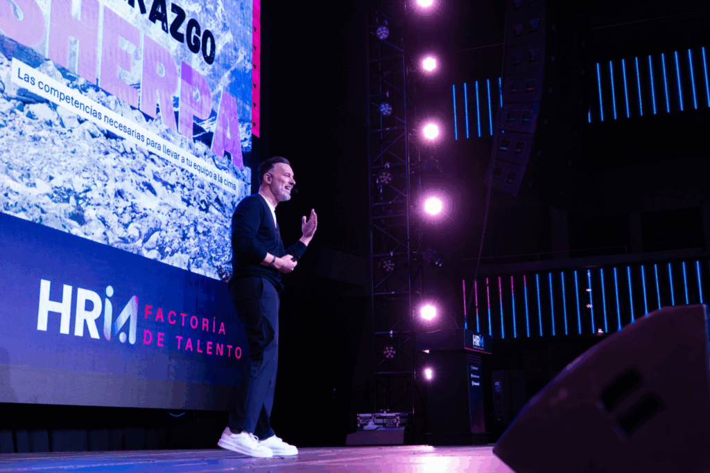 Rubén Montesinos es captado en plena sesión de formación o conferencia interactiva, guiando a un grupo de profesionales en un ambiente colaborativo. La escena transcurre en un espacio interior moderno, con luz natural y vegetación, que refuerza el enfoque humano y cercano que caracteriza sus intervenciones. Especializado en liderazgo, cultura organizacional y marca empleadora, Montesinos impulsa el desarrollo del talento desde la autenticidad y el propósito. Esta imagen es ideal para ilustrar procesos de consultoría, talleres experienciales o eventos corporativos centrados en el crecimiento humano y organizacional.