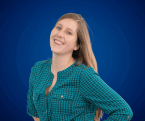 Fotografía de Sarita Infante, sonriendo con una postura relajada, sobre un fondo azul sólido. Luce una blusa de estampado geométrico en tonos verdes y negros, con el cabello suelto y expresión alegre.
