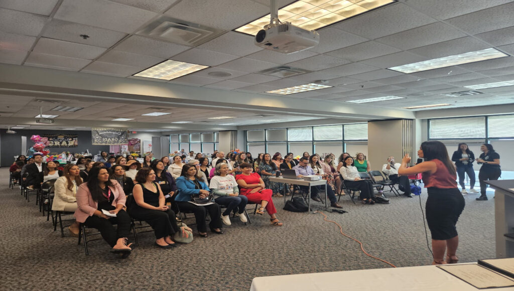 Fotografía de Yanira Puy ofreciendo una conferencia frente a un público atento en un salón iluminado con luz natural, con asistentes sentados y decoración de fondo alusiva a un evento.