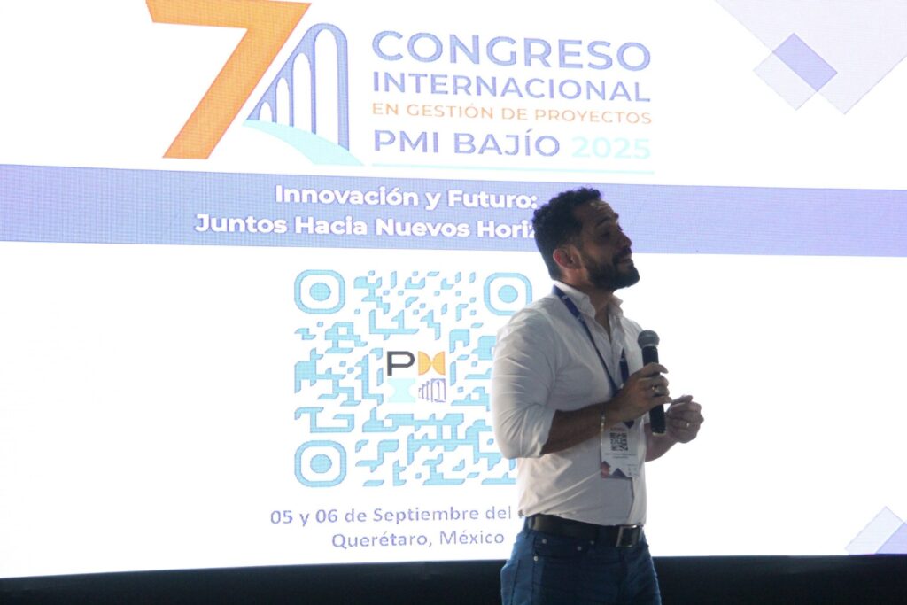 Fotografía de Jorge Moreno participando como conferencista en el 7° Congreso Internacional en Gestión de Proyectos PMI Bajío 2025 en Querétaro, México, sosteniendo un micrófono y dirigiéndose al público frente a una pantalla de proyección.