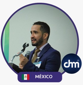 Fotografía de Jorge Moreno durante una conferencia en México, vistiendo traje azul marino y corbata mostaza, hablando con convicción frente a un micrófono.