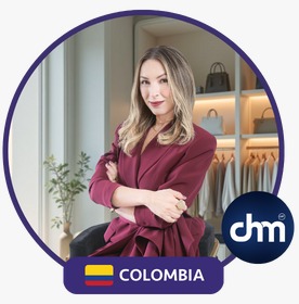 Fotografía de Yuly Giraldo en un entorno moderno tipo showroom, vestida con traje burdeos y los brazos cruzados, transmitiendo seguridad y estilo. Sello de Colombia y logotipo de CHM visibles.