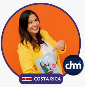Fotografía de Adriana Castro, sonriendo y señalando su libro "Viaja ligera", vestida con blazer amarillo sobre fondo naranja vibrante, con distintivo de Costa Rica y logotipo de Digital House.