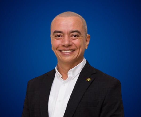 Fotografía de Julián Aguilar Estrada, posando sonriente con traje oscuro y camisa blanca sobre un fondo azul profesional.
