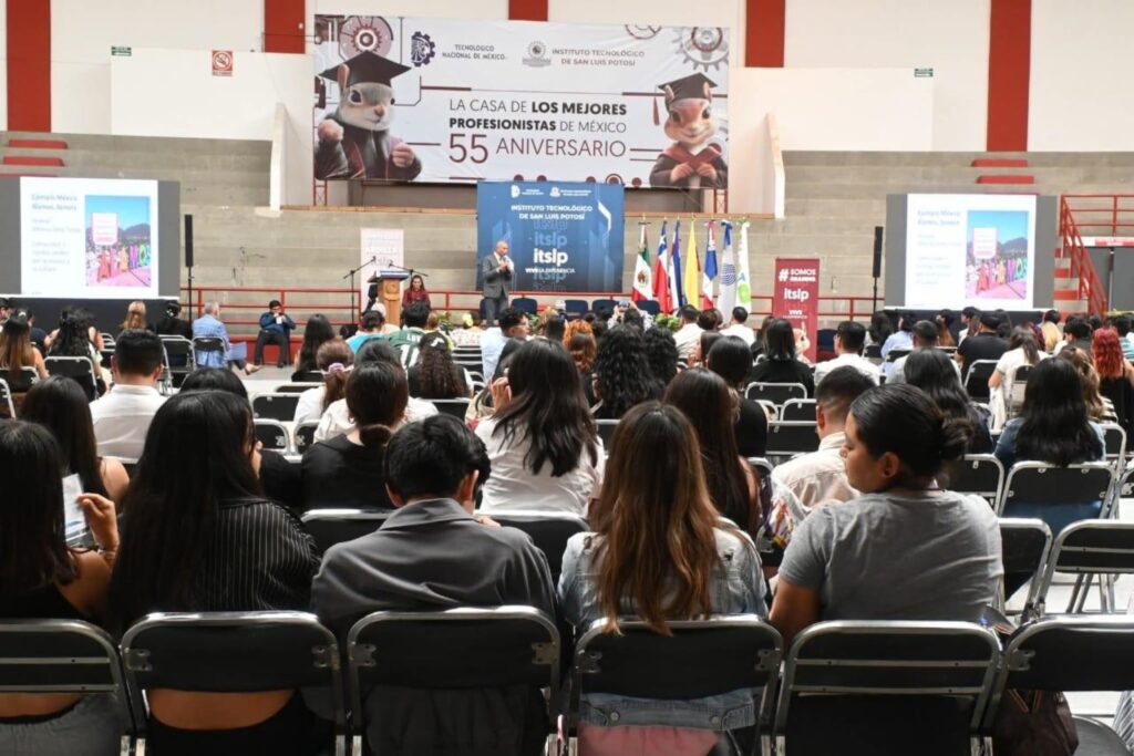 Fotografía de Julián Aguilar Estrada dando una conferencia en el auditorio del Instituto Tecnológico de San Luis Potosí, frente a una audiencia numerosa con pantallas de presentación y banderas institucionales.