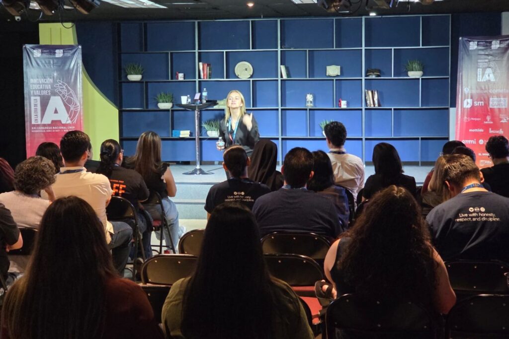 Fotografía de Nancy Reeves durante una conferencia educativa, hablando frente a una audiencia atenta, con fondo de estanterías azules y banners del XXI Congreso Nacional CNEP.