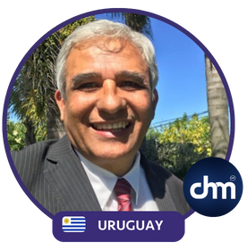 Fotografía de Roberto Patrone, sonriendo al aire libre, con traje a rayas y corbata roja, acompañado del logo de CHM y la bandera de Uruguay.