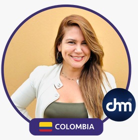 Fotografía de Linda De La Torre sonriendo frente a una pared color mostaza, con chaqueta clara y blusa verde oliva, acompañada del logotipo de CHM y la bandera de Colombia.