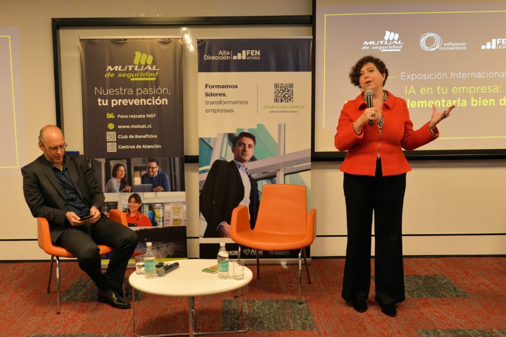 Fotografía de Jennyfer Salvo dando una conferencia sobre inteligencia artificial en empresas, de pie con micrófono en mano, junto a un panelista sentado y banners institucionales de fondo.