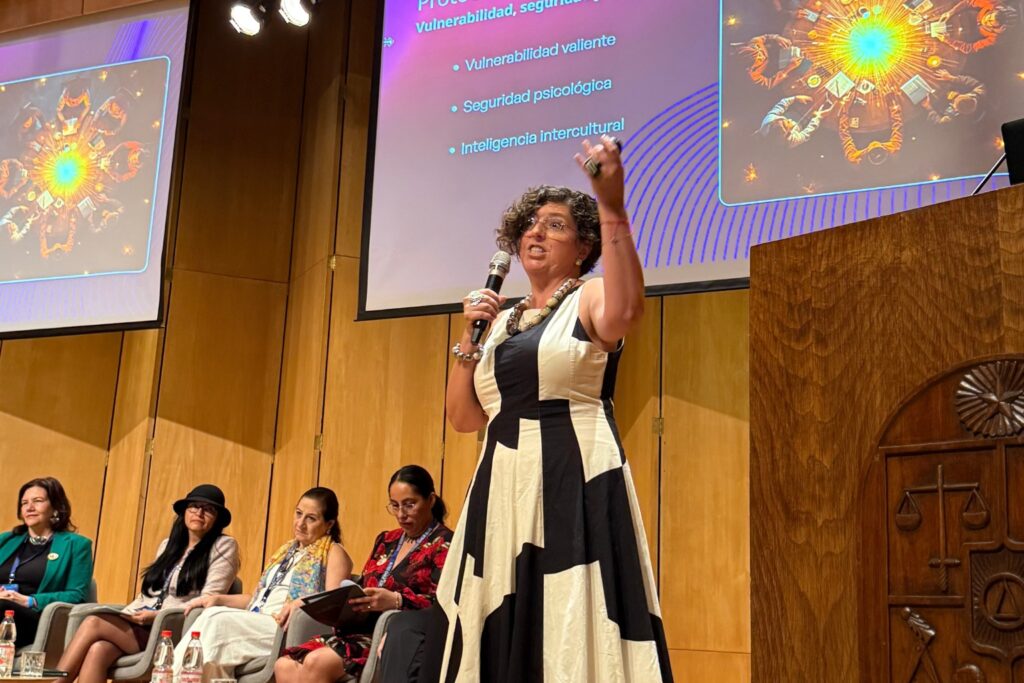 Fotografía de Jennyfer Salvo dando una ponencia apasionada en un auditorio, con micrófono en mano y presentaciones proyectadas sobre vulnerabilidad, seguridad psicológica e inteligencia intercultural.